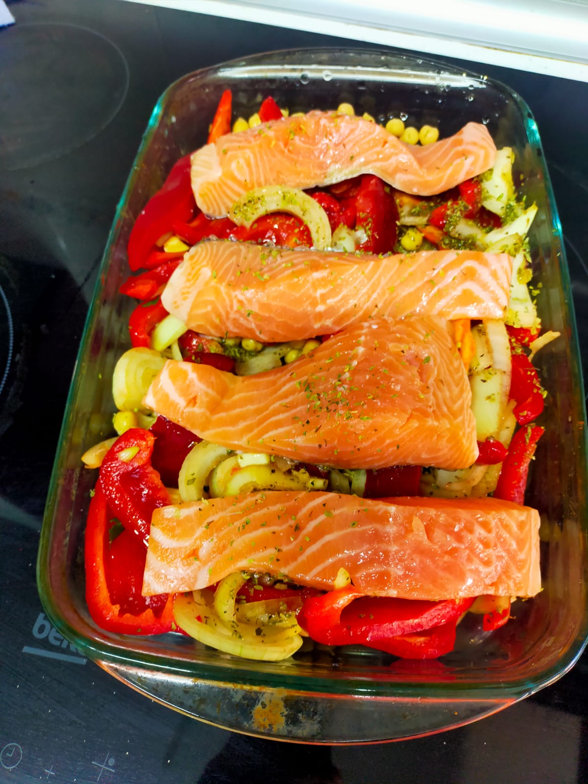 Gran bandeja de salmón con pimientos rojos lista para ser hecha al horno.